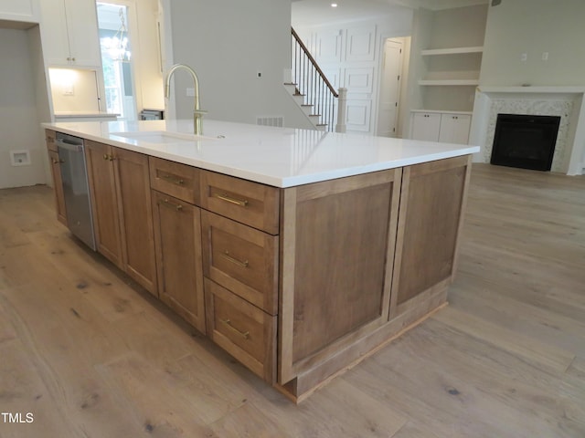 kitchen featuring stainless steel dishwasher, light wood-style flooring, brown cabinetry, and a sink