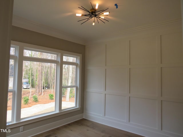 spare room with a chandelier, a decorative wall, light wood-type flooring, and ornamental molding