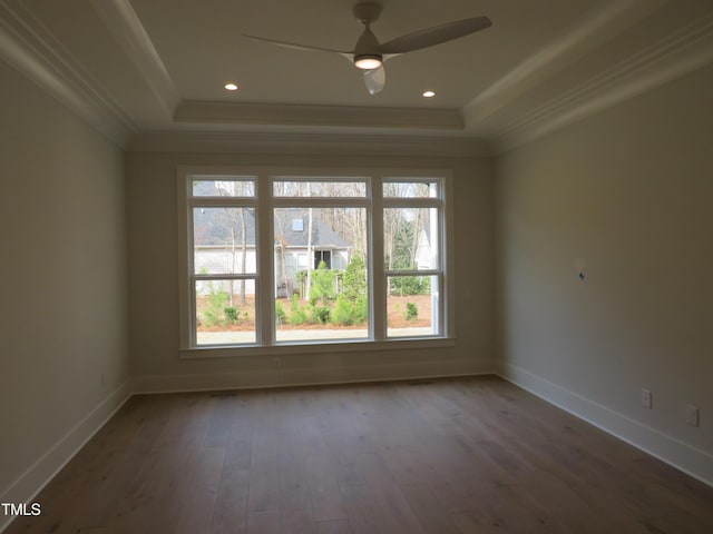 empty room with wood finished floors, a raised ceiling, and ornamental molding