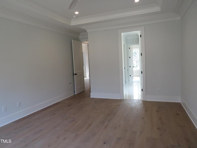 spare room with a tray ceiling, wood finished floors, and ornamental molding