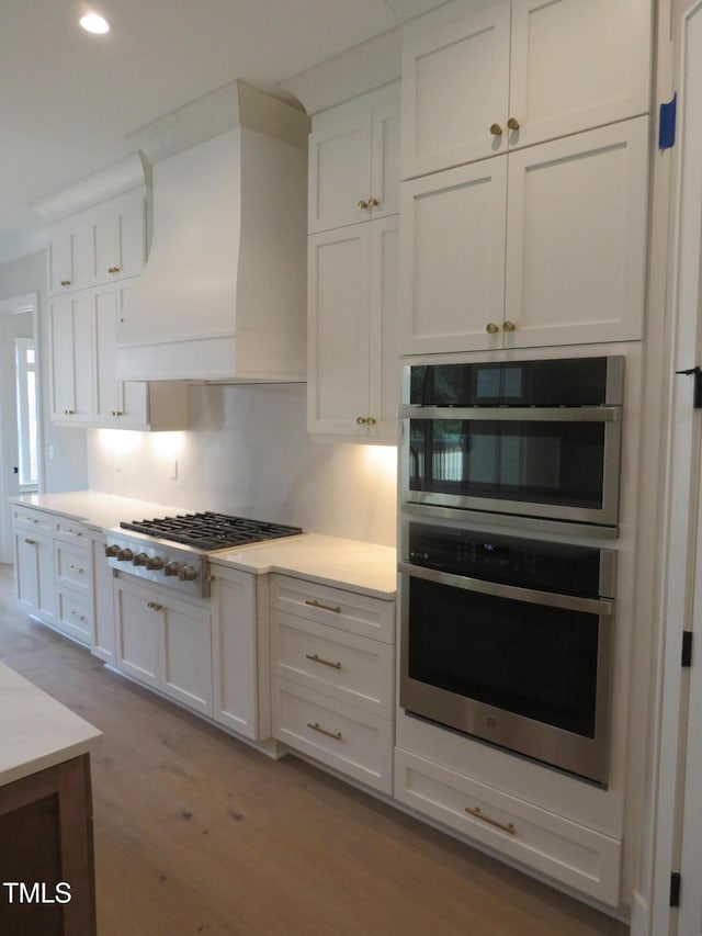 kitchen featuring premium range hood, gas stovetop, white cabinetry, double oven, and light countertops