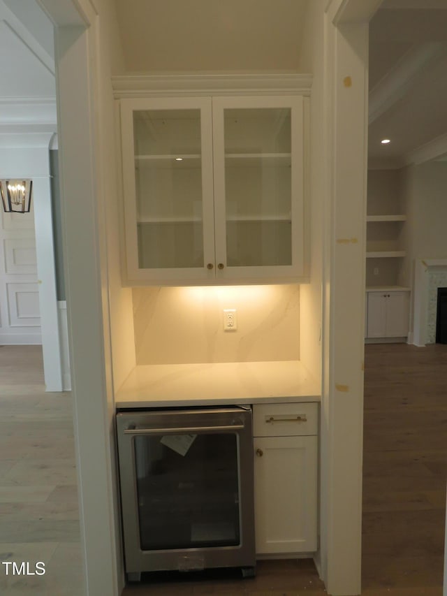 room details with beverage cooler, crown molding, an inviting chandelier, and wood finished floors