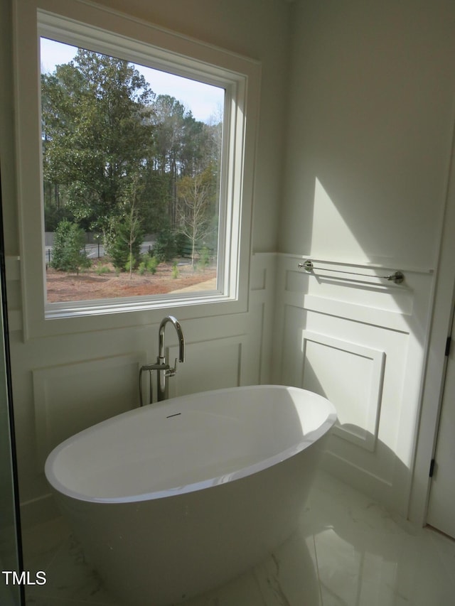 full bath featuring a wainscoted wall, a soaking tub, marble finish floor, and a decorative wall