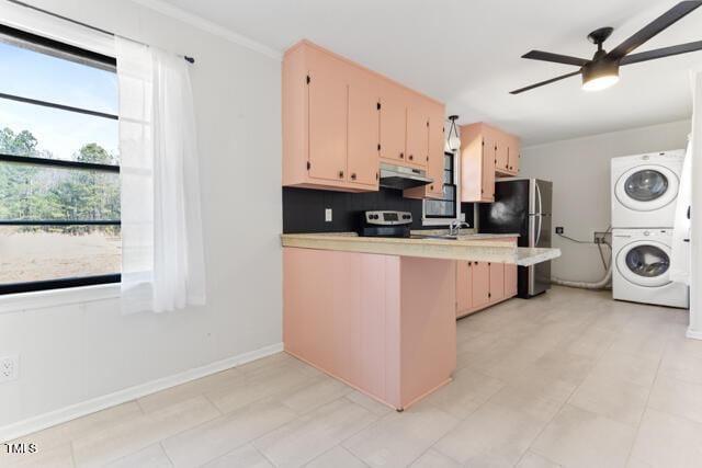 kitchen featuring stacked washer and clothes dryer, a ceiling fan, under cabinet range hood, a peninsula, and light countertops