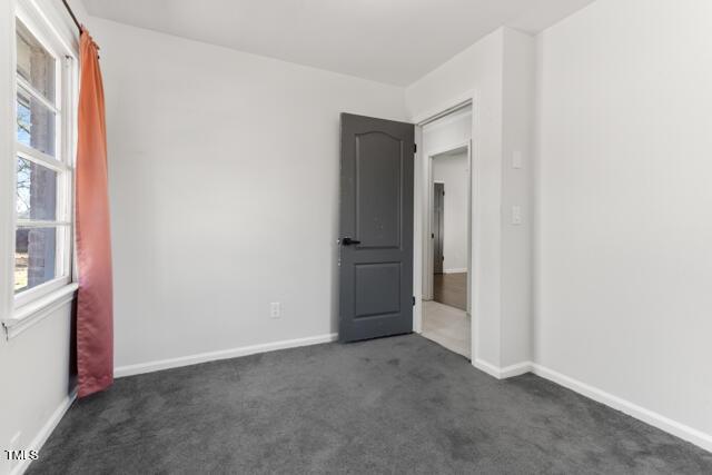 spare room with a wealth of natural light, dark carpet, and baseboards