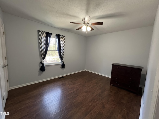 unfurnished room with baseboards, visible vents, ceiling fan, dark wood-type flooring, and a textured ceiling