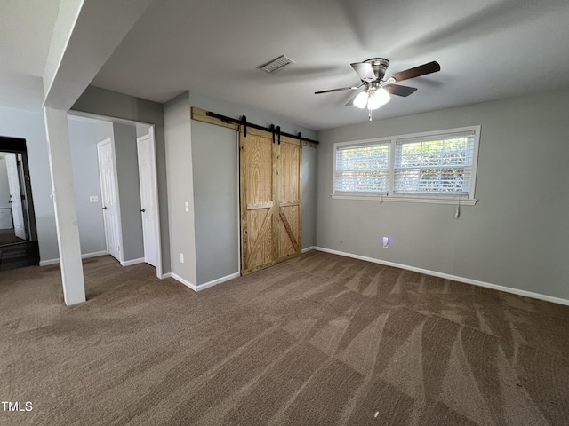 unfurnished bedroom with baseboards, visible vents, ceiling fan, a barn door, and carpet flooring