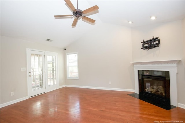 unfurnished living room featuring hardwood / wood-style floors, baseboards, visible vents, a fireplace with flush hearth, and vaulted ceiling