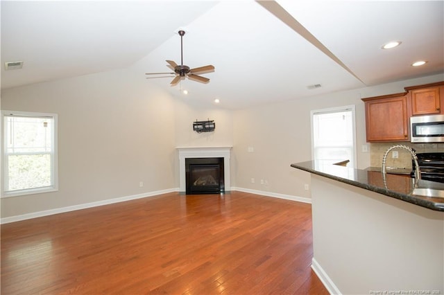 unfurnished living room with wood finished floors, visible vents, lofted ceiling, ceiling fan, and a glass covered fireplace