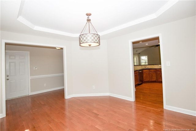 empty room featuring baseboards, a tray ceiling, a sink, light wood-style floors, and crown molding