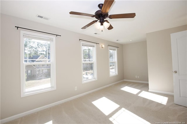 spare room featuring ceiling fan, light colored carpet, visible vents, and baseboards