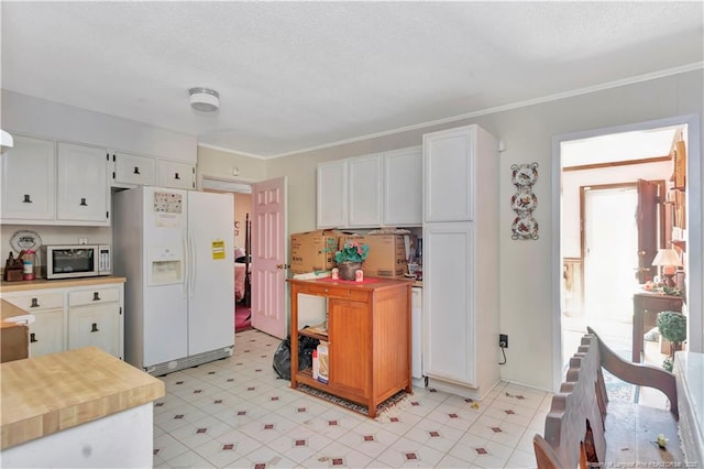 kitchen featuring stainless steel microwave, light floors, ornamental molding, white fridge with ice dispenser, and white cabinets