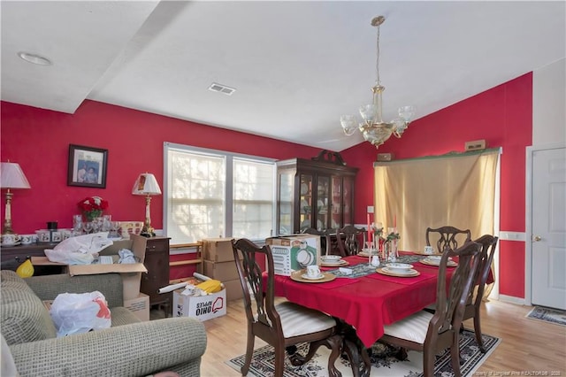 dining area with a chandelier, visible vents, vaulted ceiling, and wood finished floors