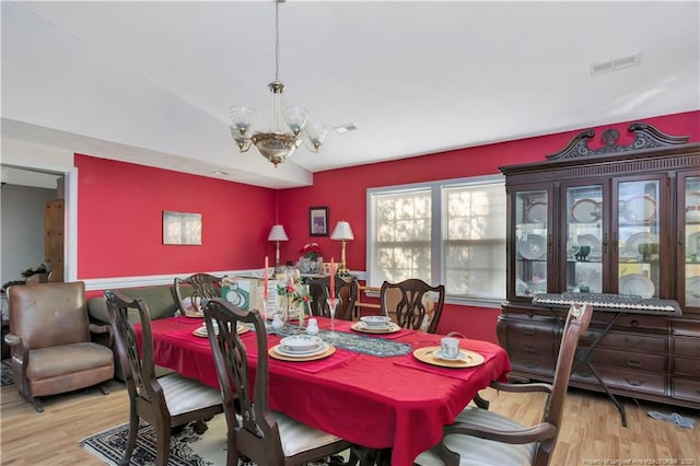 dining space with lofted ceiling, wood finished floors, visible vents, and a chandelier