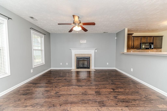 unfurnished living room with a fireplace with flush hearth, dark wood-style floors, visible vents, and ceiling fan