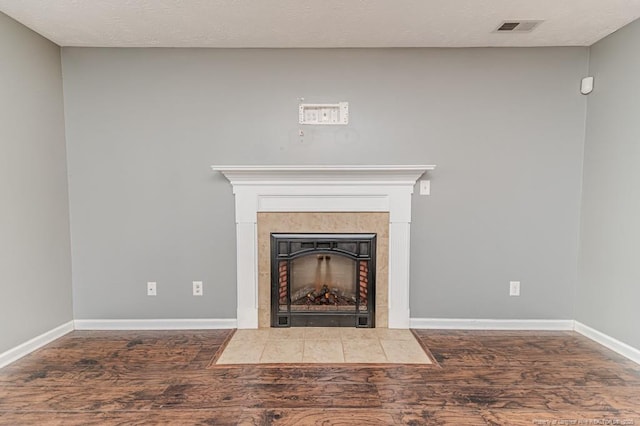 details featuring a tiled fireplace, wood finished floors, visible vents, and baseboards