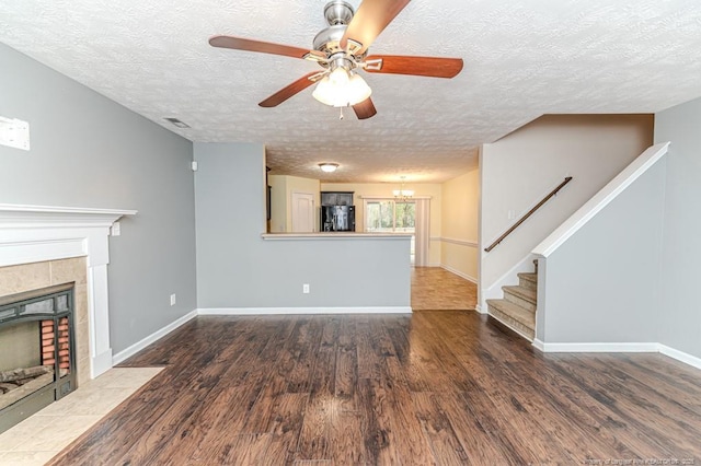 unfurnished living room featuring wood finished floors, baseboards, a fireplace, stairs, and ceiling fan with notable chandelier