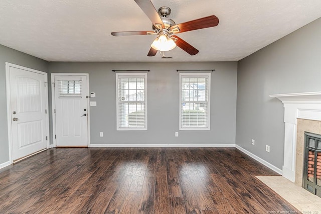 unfurnished living room featuring a ceiling fan, a textured ceiling, wood finished floors, a fireplace, and baseboards