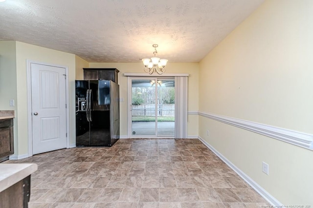 unfurnished dining area featuring an inviting chandelier, baseboards, and a textured ceiling