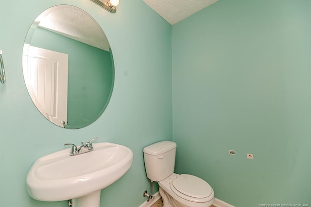 half bath with a textured ceiling, toilet, baseboards, and a sink