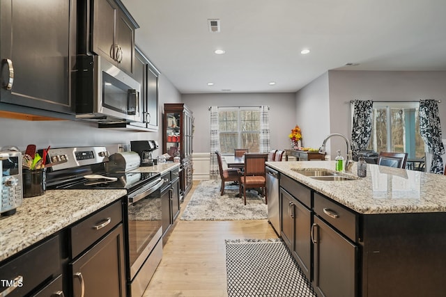 kitchen with visible vents, a kitchen island with sink, a sink, stainless steel appliances, and light wood finished floors