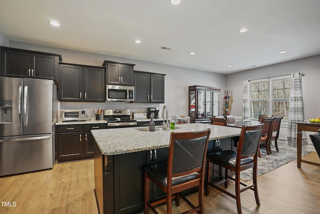 kitchen featuring light wood finished floors, visible vents, a breakfast bar, appliances with stainless steel finishes, and a sink