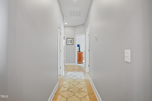 corridor with baseboards, visible vents, and light wood finished floors