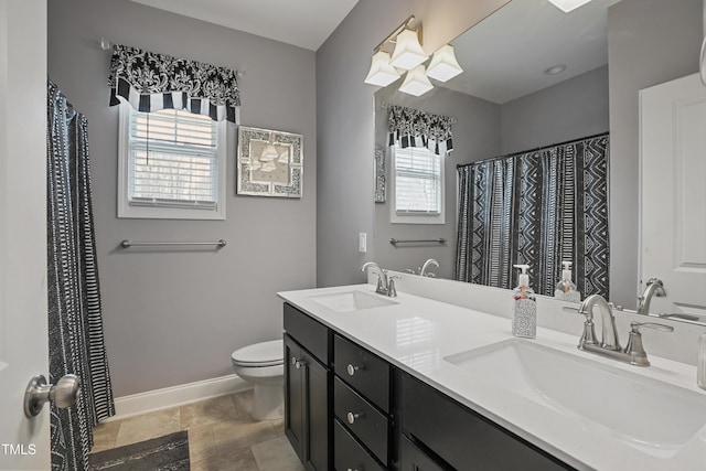 bathroom with double vanity, toilet, baseboards, and a sink