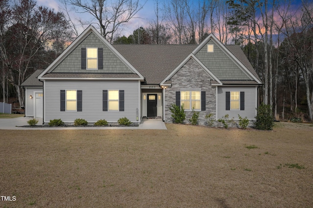 view of front of property featuring stone siding, a yard, and roof with shingles