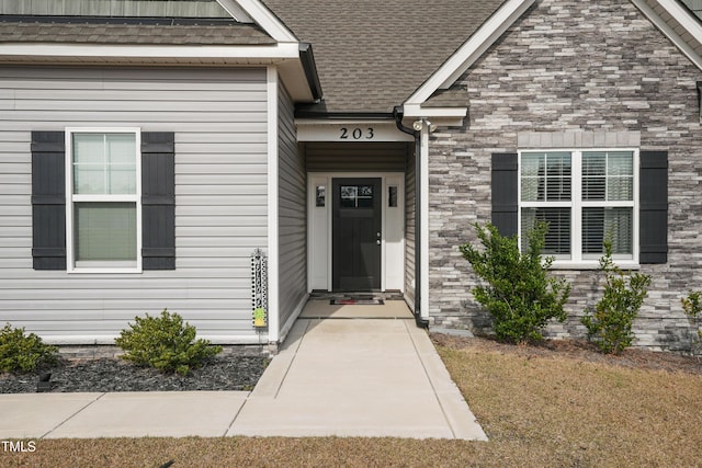 view of exterior entry with stone siding and a shingled roof