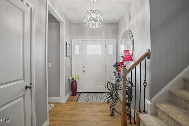 foyer entrance with a chandelier, stairs, baseboards, and wood finished floors