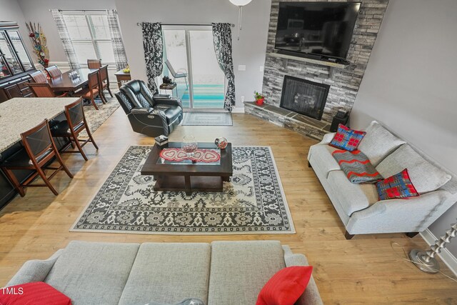 living room with baseboards, a stone fireplace, and wood finished floors