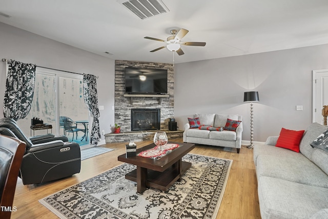 living area with visible vents, wood finished floors, a stone fireplace, and ceiling fan