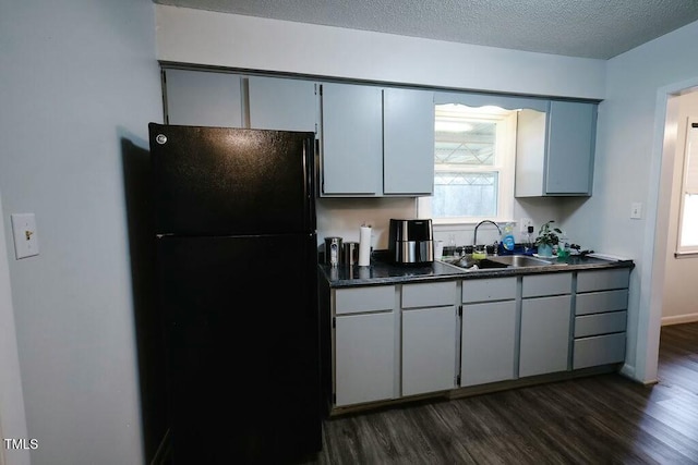 kitchen with dark countertops, dark wood-style flooring, freestanding refrigerator, and a sink