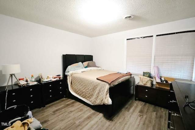 bedroom featuring visible vents, a textured ceiling, and wood finished floors