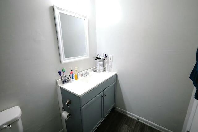 half bathroom with baseboards, toilet, wood finished floors, and vanity