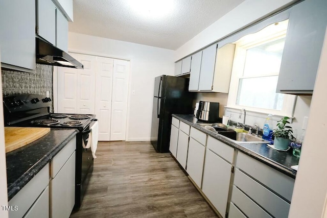 kitchen featuring dark wood-style floors, black appliances, under cabinet range hood, a textured ceiling, and dark countertops