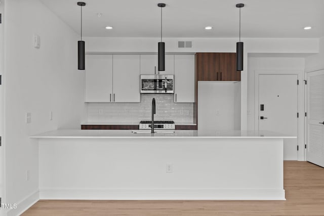 kitchen with stainless steel microwave, visible vents, light wood-style flooring, and light countertops