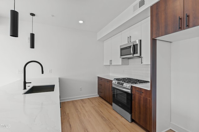 kitchen featuring visible vents, light wood-style flooring, a sink, appliances with stainless steel finishes, and decorative backsplash