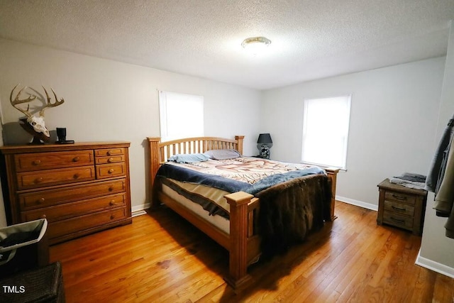 bedroom with light wood finished floors, a textured ceiling, and baseboards