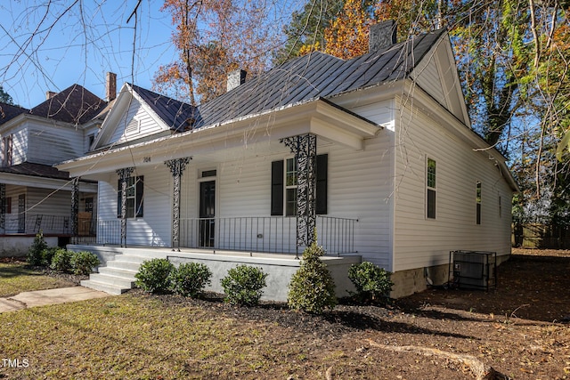 view of front of home with central air condition unit, metal roof, covered porch, and a chimney