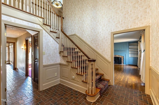 staircase with a wainscoted wall, a fireplace, a high ceiling, brick floor, and a decorative wall