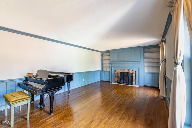 living area with dark wood-style floors, wainscoting, a brick fireplace, and built in shelves