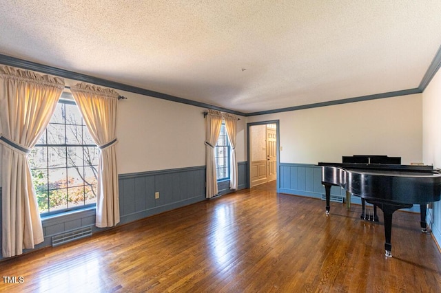 sitting room with a textured ceiling, wood finished floors, visible vents, and wainscoting