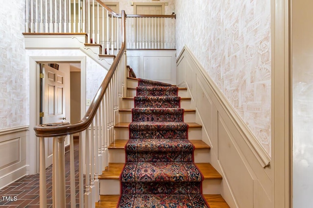 staircase with wallpapered walls, a decorative wall, brick floor, and a wainscoted wall