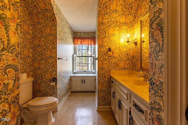 bathroom with vanity, baseboards, wallpapered walls, a textured ceiling, and toilet