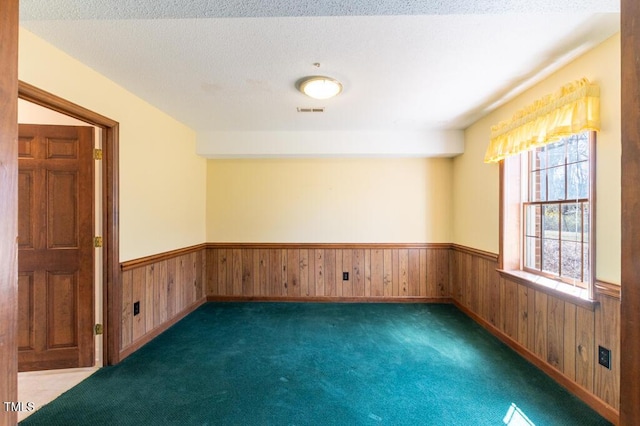 carpeted spare room featuring a wainscoted wall, wood walls, a textured ceiling, and visible vents