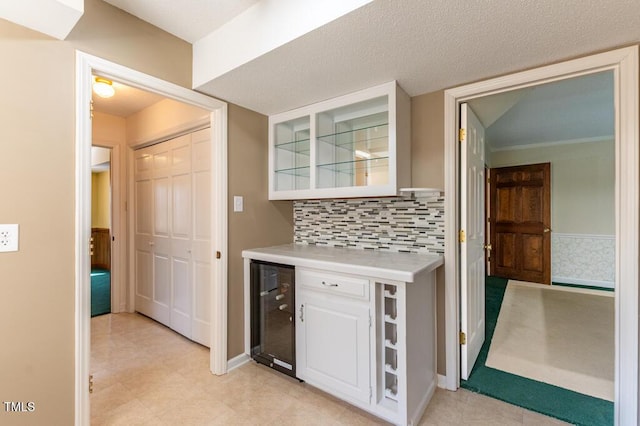 interior space featuring light countertops, wine cooler, glass insert cabinets, white cabinetry, and tasteful backsplash