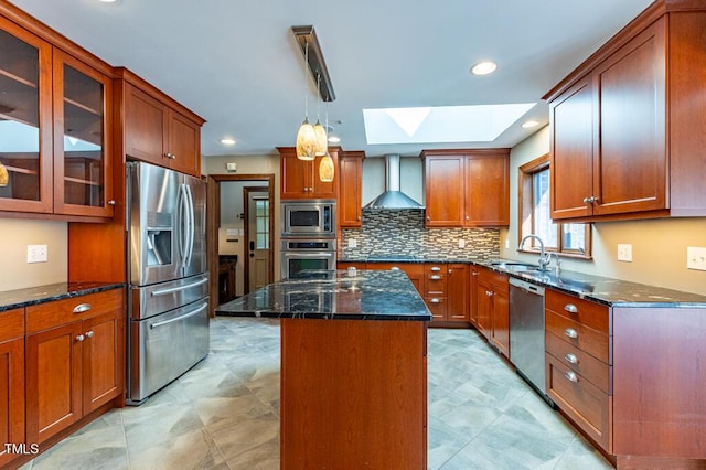 kitchen with dark stone counters, a skylight, a sink, appliances with stainless steel finishes, and wall chimney exhaust hood