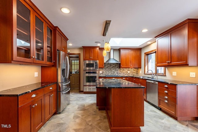 kitchen with a kitchen island, a sink, appliances with stainless steel finishes, wall chimney range hood, and backsplash